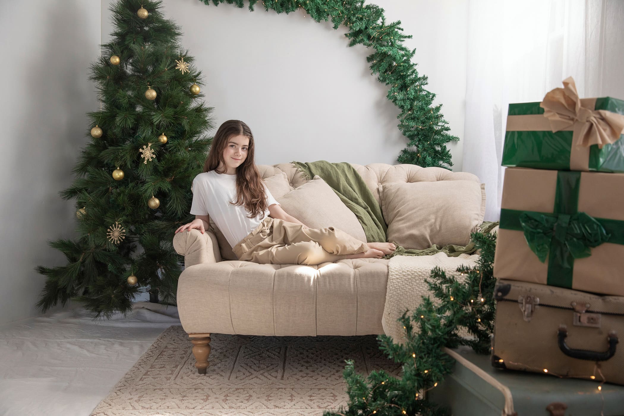 Older girl in a white t-shirt sitting on a tufted sofa beside a Christmas tree