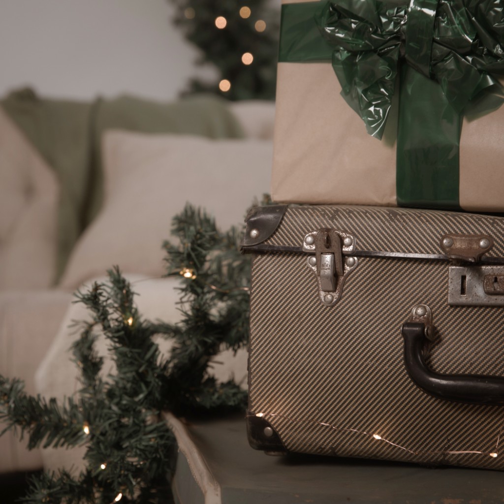 Vintage suitcase stacked with a kraft-wrapped gift and a green ribbon beside lit pine greenery