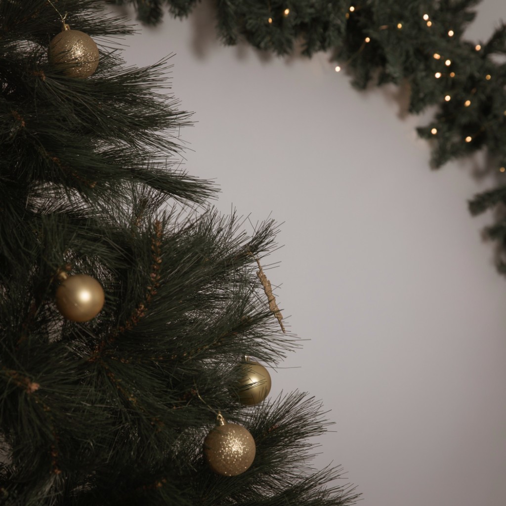 Gold and glitter baubles on a pine Christmas tree with a lit garland along the top