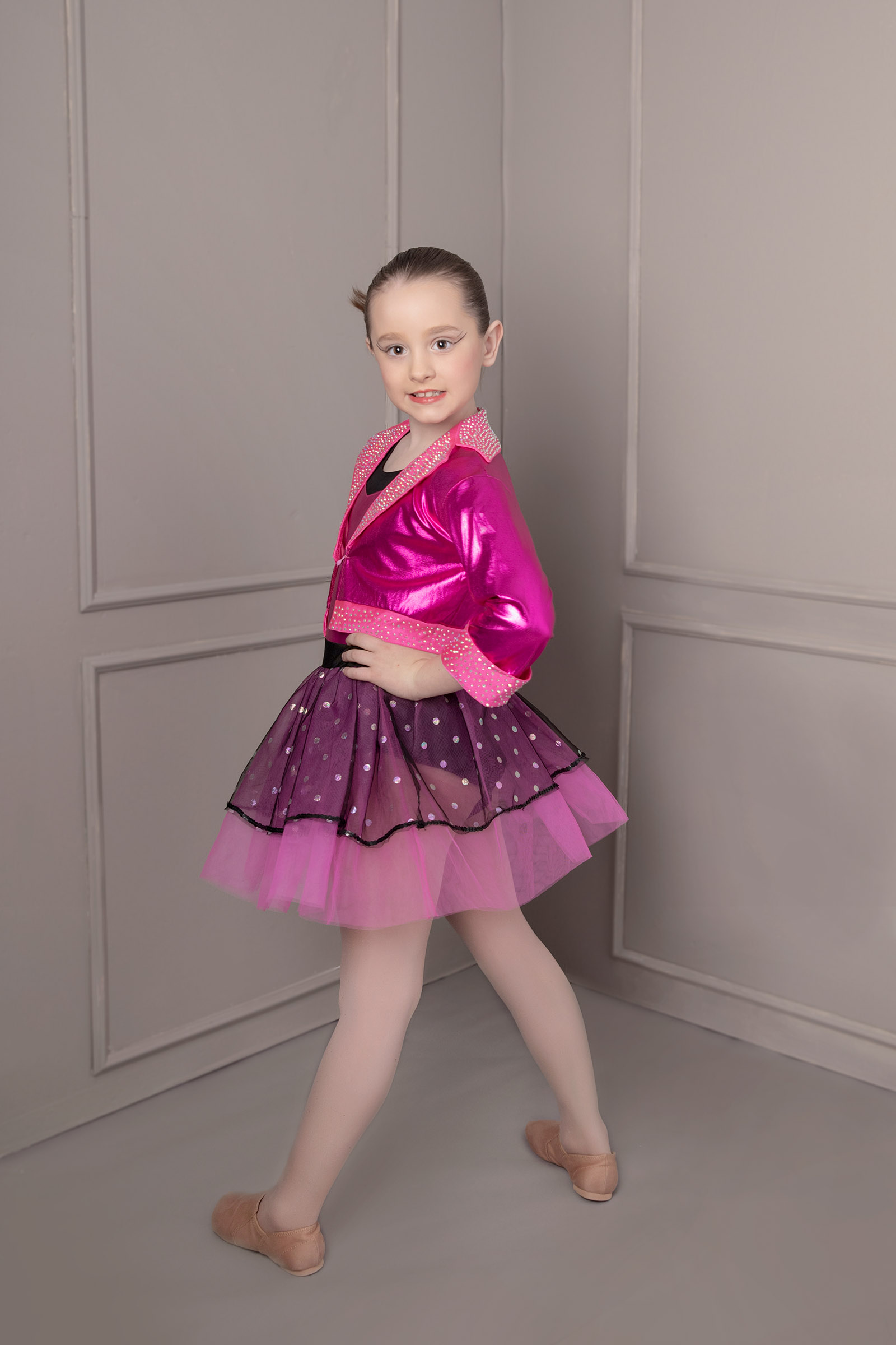 Young dancer in a pink jacket and tutu posing in a studio