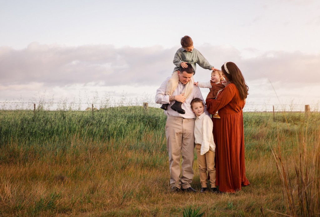Family with three children photographed in a paddock at golden hour