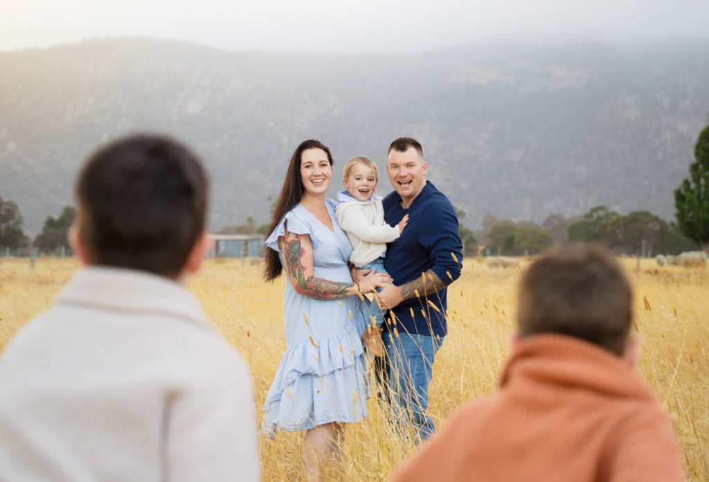 Family with children photographed in a grassy paddock, with ranges in the distance
