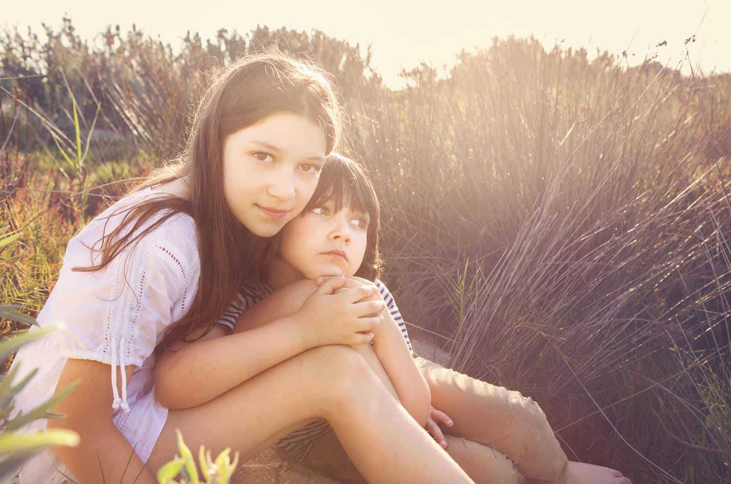 Two children photographed together in a sunlit field during a family portrait session