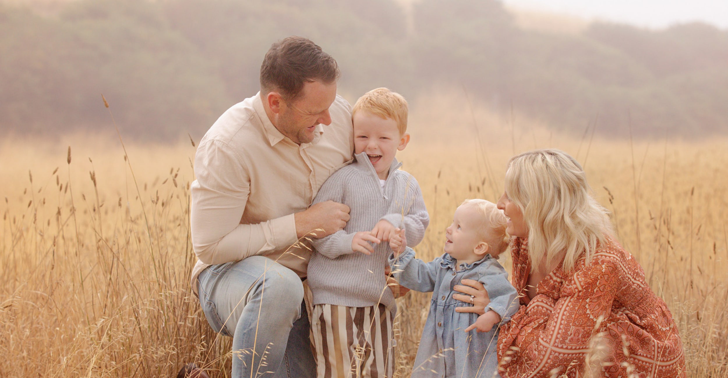 Family with two children photographed in tall golden grass at sunset