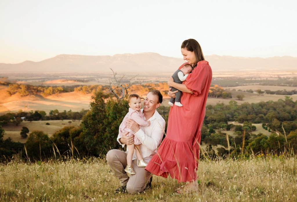 Family with two children photographed on a grassy hill at sunrise, with ranges in the distance