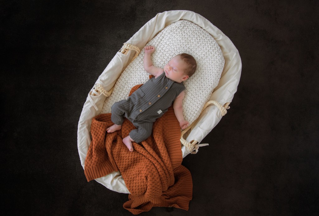 Newborn sleeping in a woven basket with a knit blanket