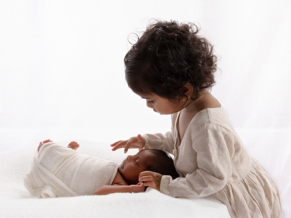 Older child gently touching a newborn sibling during a portrait session