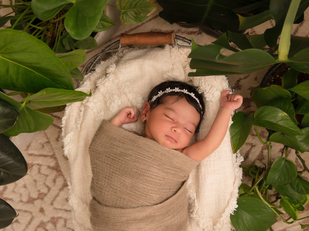 Newborn baby stretching in a woven basket during a portrait session
