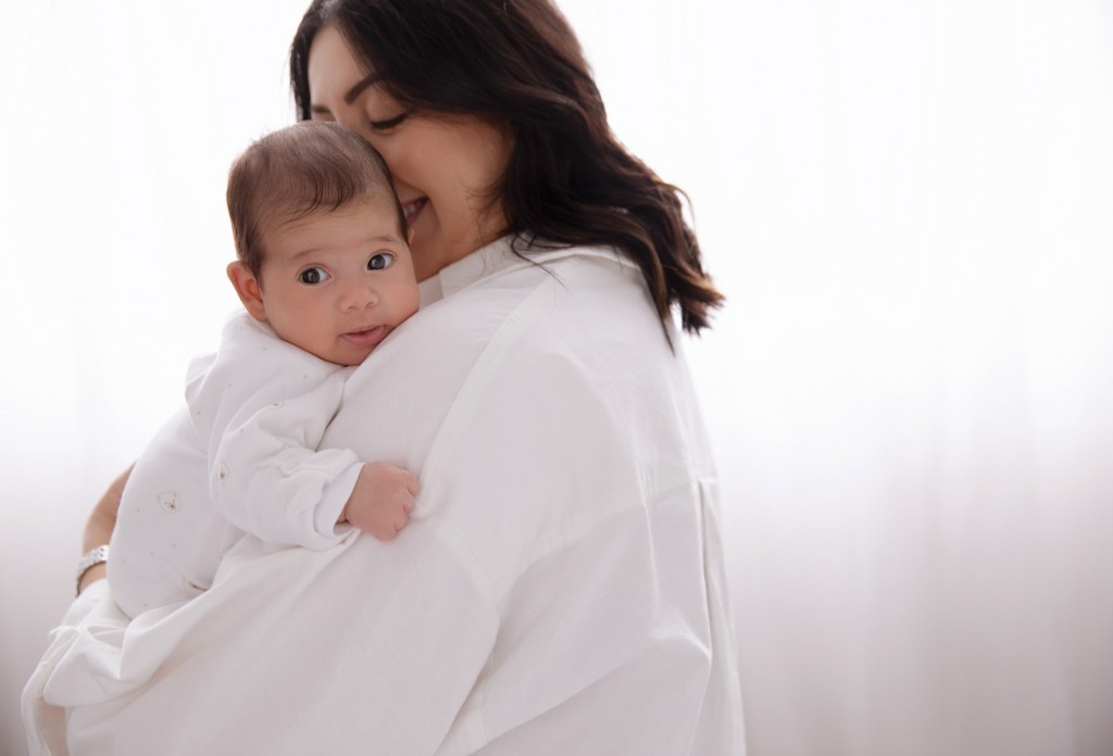 Mother holding a baby in a bright studio, with the baby looking toward the camera